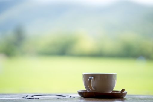 A selective focus shot of a cup of coffee on a wooden table outdoors