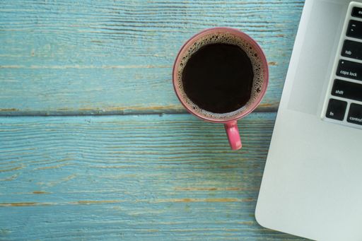 A top view of a cup of brewed coffee beside a laptop on an old wooden surface