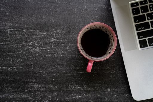 An overhead shot of a cup of coffee next to a laptop on a desk