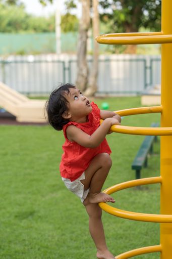 A vertical shot of a Southeast Asian toddler girl in a playground outdoors