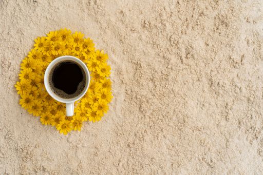 A top view of a cup of coffee surrounded by yellow flowers on a rock surface with space
