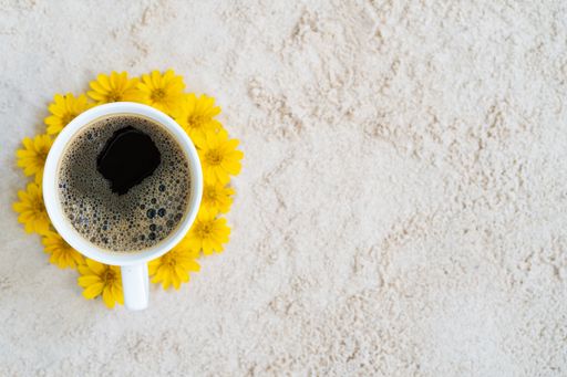 A top view of a cup of coffee surrounded by yellow flowers on a rock surface with space