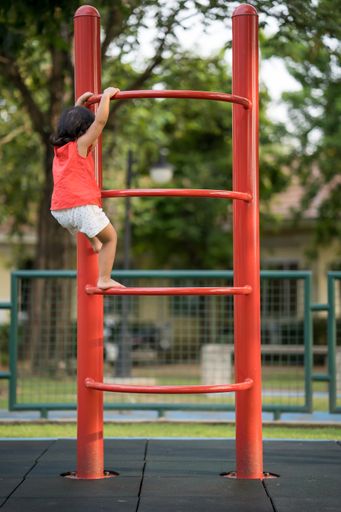 A rear view of a little girl climbing on a red steel ladder in a park