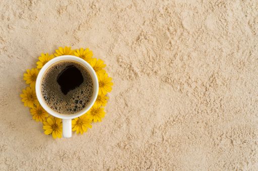 A top view of a cup of coffee surrounded by yellow flowers on a rock surface with space