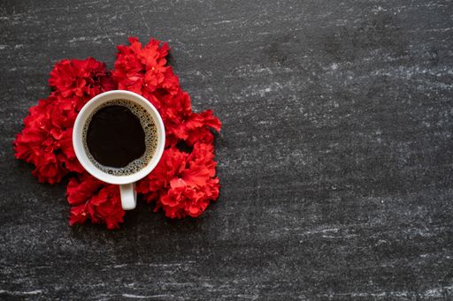 An overhead shot of a cup of coffee surrounded by red flowers on a table