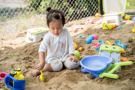A cute little Southeast Asian girl playing with sand at the playground