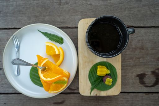 A top view of a cup of coffee and fresh orange slices on a wooden table