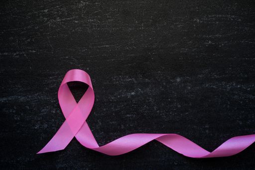 A closeup of a pink ribbon on a black surface - breast cancer awareness