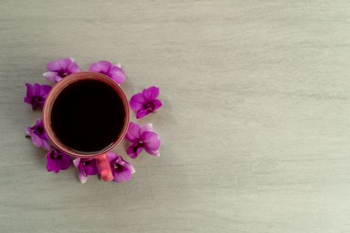 A top view of a cup of coffee surrounded by purple flowers on a wooden surface with copy space