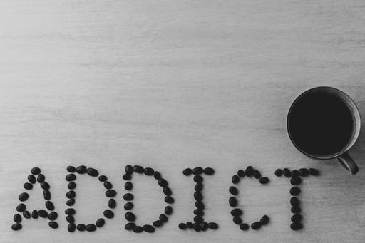A top view of roasted beans formed as addict text beside a cup of coffee with copy space