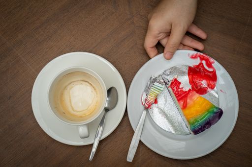 A closeup of an empty coffee cup with a hand holding a plate with a colorful piece of cake.