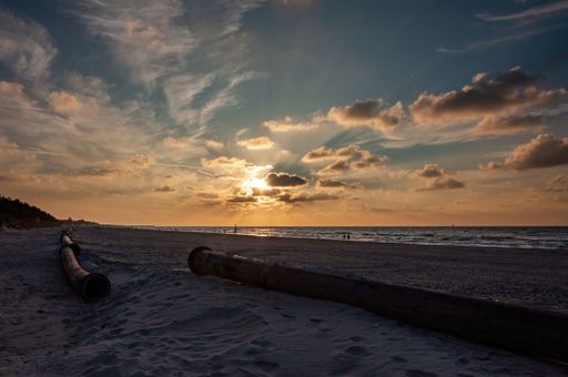 A serene beach scene at sunset featuring a dramatic sky filled with clouds