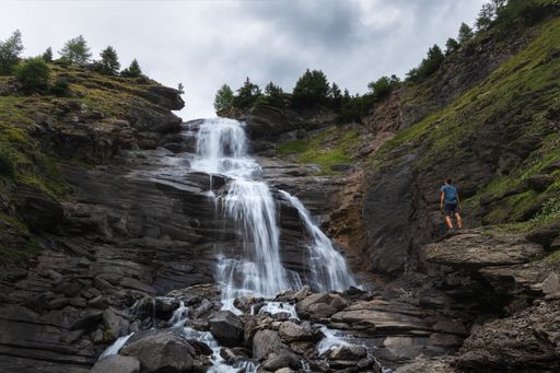 Summer landscape view of a hiker silhouette standing on a rock in front of a waterfall