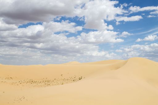 A serene desert landscape with sand dunes under a partly cloudy blue sky.