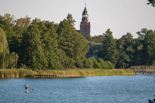 A serene lake scene with a paddleboarder and a historic tower in the background surrounded by lush greenery.