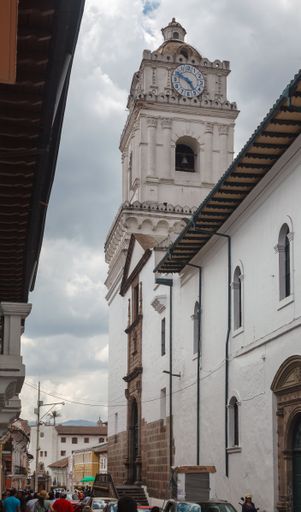 A vertical shot of the clocktower of the Basilica of Our Lady of Mercy under a cloudy sky in a historic downtown district
