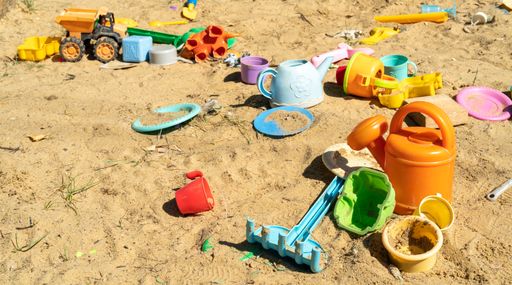 A closeup shot of multi-colored children's plastic toys in the sand on a beach