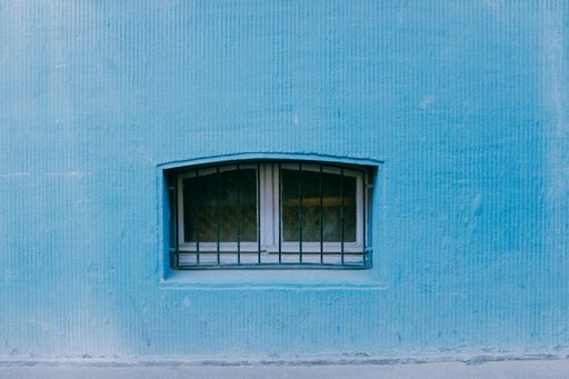 A closeup shot of a small window with metal bars in a blue painted wal