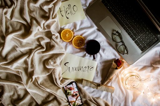 A Summer written on paper near the laptop and phone with a cup of coffee and juicy orange on the bed