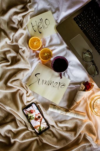 A Summer written on paper near the laptop and phone with a cup of coffee and juicy orange on the bed