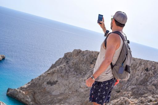 A back view of a young male tourist taking photos on his phone on a cliffy shoreline