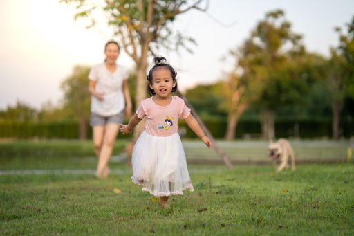 A cute Asian female child playing in the grass with her mother and pet behind her