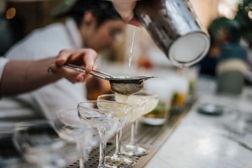 A closeup shot of a barman making margaritas with four glasses set in line