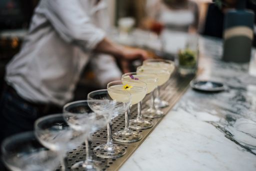 A closeup shot of a barman making margaritas with a number of glasses set in line