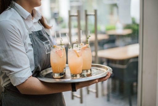 A closeup shot of a waiter serving cocktail with fresh oranges on a silver tray