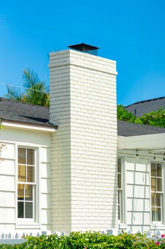 A vertical shot of a white brick house with a chimney under a clear blue sky in a rural town