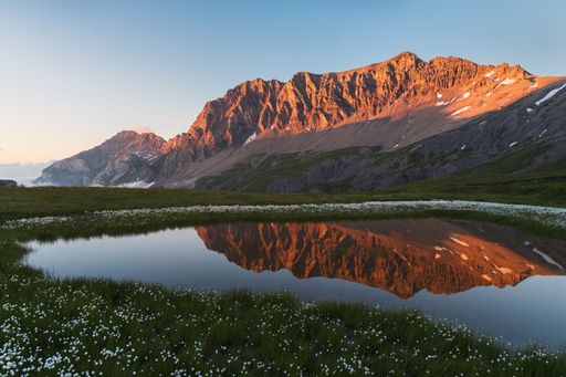 Summer sunset landscape view of an illuminated orange mountain range reflecting in a small pond