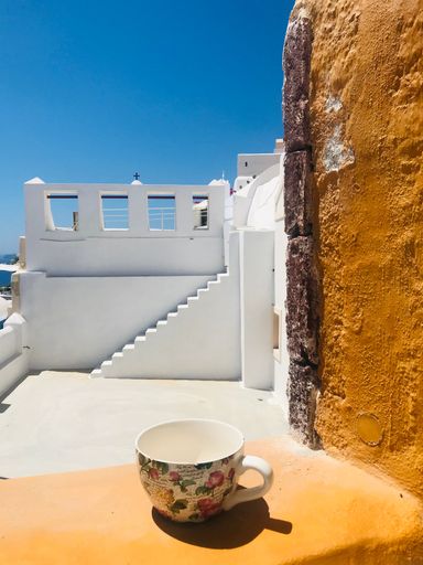 A closeup vertical shot of an empty mug on a table, with coastal white house in the background in Santorini island on a sunny day, Greece