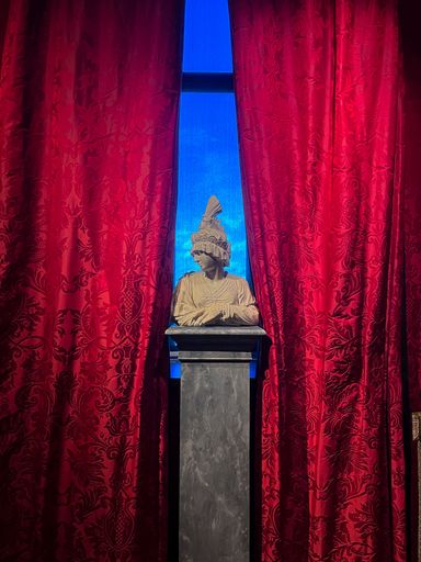 A vertical shot of statue of a man in front of a red curtain in a museum in Philadelphia