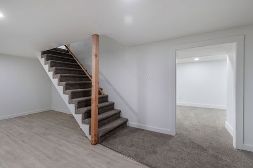 An interior view of a staircase in a renovated empty room with white walls and wooden parquet flooring, illuminated with bright natural light