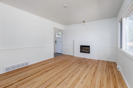 An interior view of a renovated empty room with wooden parquet flooring and white walls with big glass window