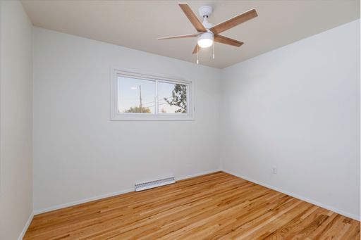 An interior view of a renovated empty room with wooden parquet flooring, ceiling fan and white walls with small glass window