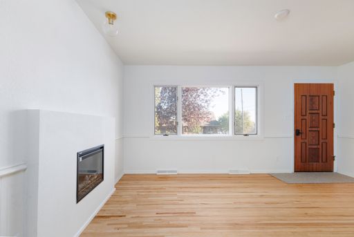 An interior view of a renovated empty room with wooden parquet flooring and white walls, with big glass window and wooden door in the background