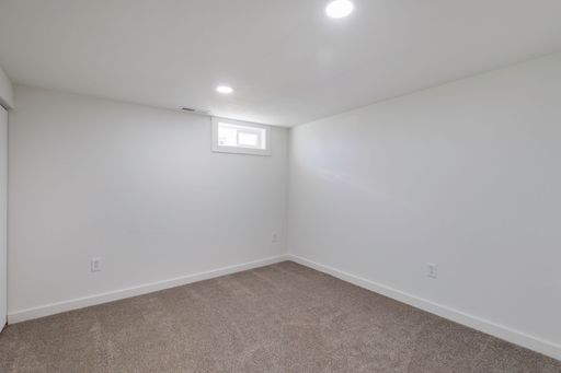 An interior view of a new, renovated empty room, with carpet flooring and small window on the white wall, illuminated with bright light