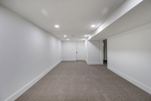 An interior view of a new, renovated empty room, with carpet flooring, white walls, illuminated with bright light