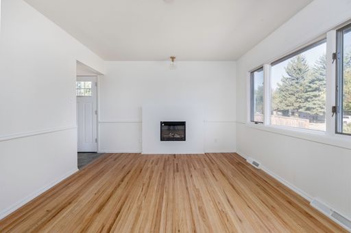 An interior view of a new, renovated empty room with wooden parquet flooring and white walls with big glass window with a scenic view