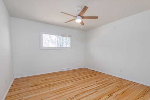 An interior view of a new, renovated empty room with wooden parquet flooring, white walls and ceiling fan in bright natural light
