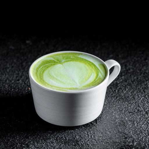 A close-up shot of a matcha latte with beautiful latte art in a white cup against a dark background.