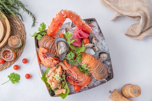 A top view of a fresh seafood platter on ice, featuring lobster, crab legs, shrimp, oysters, and clams, garnished with herbs and cherry tomatoes.