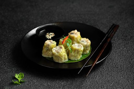 A plate of steamed dumplings served with soy sauce and garnished with cilantro on a dark textured background.