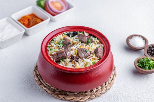 A delicious serving of biryani in a red pot, accompanied by side dishes and spices on a textured white background.