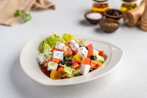 A fresh Greek salad with feta cheese, tomatoes, cucumbers, olives, and lettuce served in a white bowl on a light background.