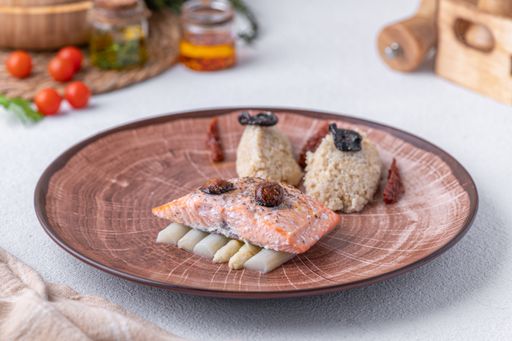 A gourmet plate featuring baked salmon on a bed of asparagus, served with quinoa and garnished with dried tomatoes and truffles.