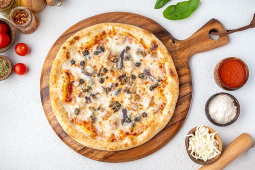 Top view of a delicious pizza with mushrooms and capers on a wooden board surrounded by ingredients on a white background.