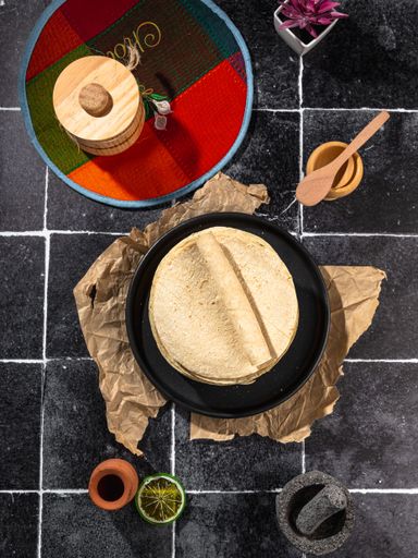 Overhead view of traditional Mexican tortillas on a black plate with various kitchen items on a tiled surface