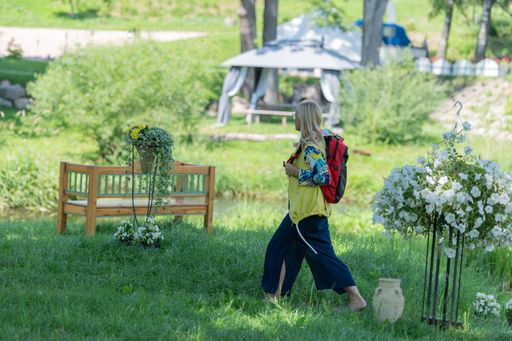 A woman with a colorful backpack walks through a lush green park on a sunny day